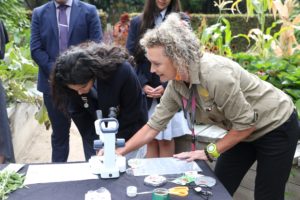 A botanist and school student examining specimens through a microscope in a garden setting.